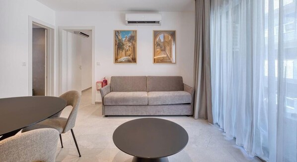 Un saló modern amb un sofà, una taula de centre rodona i una zona de dinar amb cadires. Hi ha un extintor a la paret, i dos quadres penjats sobre el sofà.