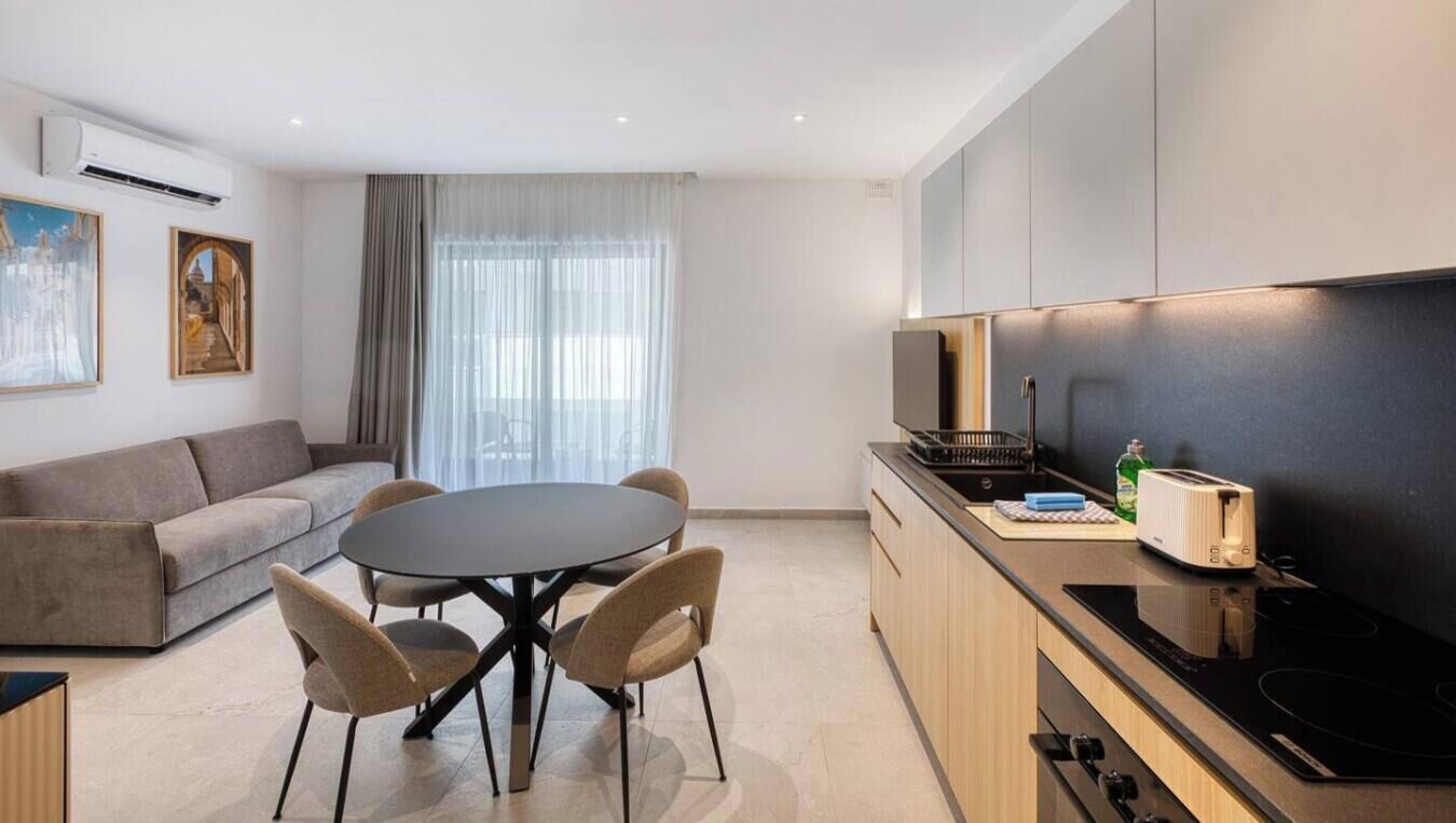 Una cucina moderna con zona pranzo, che include un tavolo rotondo e sedie, un divano e un'ampia finestra con tende.