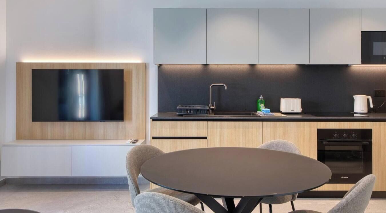 Una cucina moderna con una TV a schermo piatto montata a parete, un forno integrato e un'area pranzo con tavolo e sedie rotonde.