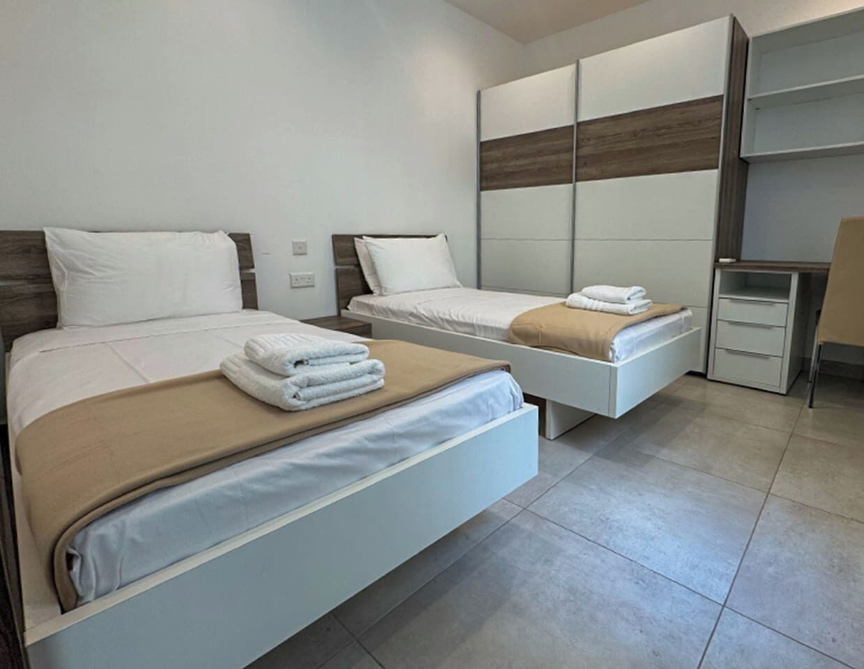 Habitación de hotel con dos camas, un armario y un escritorio pequeño.