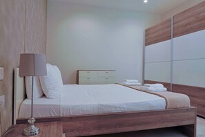 A neatly made bed with a wooden headboard, a bedside table with a lamp, and a small bedside drawer. - Gozo Countryside Views | 3 BR Apt. Sannat w/AC (Sannat)
