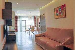 A modern living room with a sofa, a dining table with chairs, and a staircase leading to an upper floor. - Gozo Countryside Views | 3 BR Apt. Sannat w/AC (Sannat)