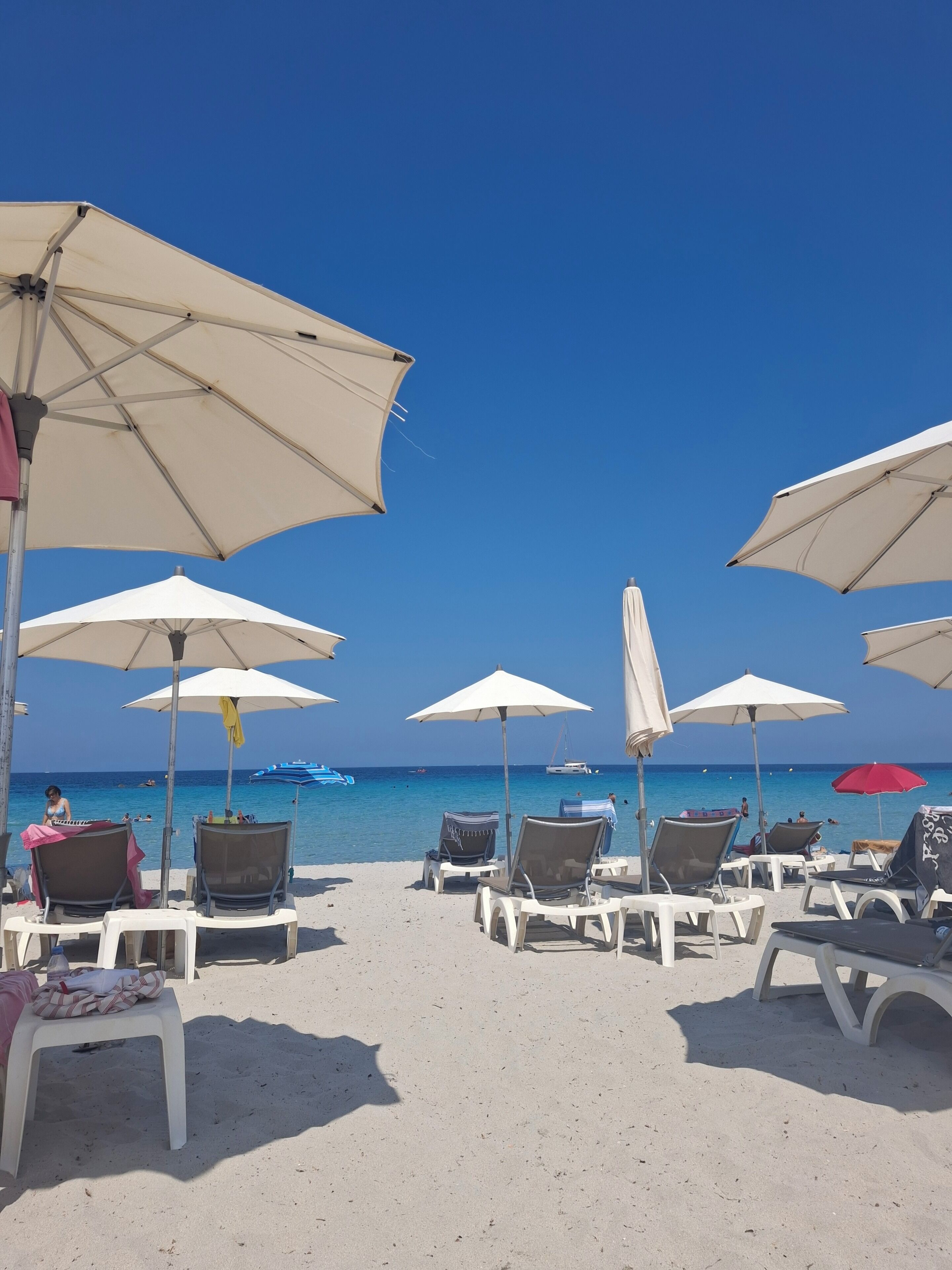 A beach with white lounge chairs and umbrellas, a clear blue sky, and the ocean in the background.