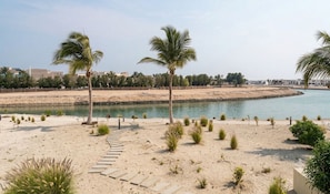 A sandy beach with palm trees and a water body. - Hawana Lagoons (ولاية طاقة،)