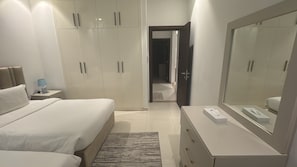 A modern bedroom with a large bed, bedside tables, a dresser, a mirror, and a walk-in closet. - Hawana Lagoons (ولاية طاقة،)