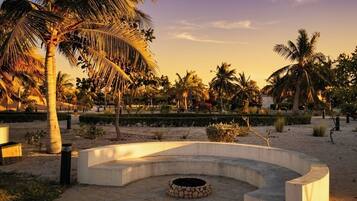 A circular outdoor seating area with a fire pit, surrounded by palm trees and a landscaped garden.
