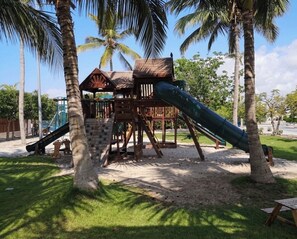 A playground with a slide and climbing structures, surrounded by palm trees and a clear sky. - Hawana Lagoons (ولاية طاقة،)