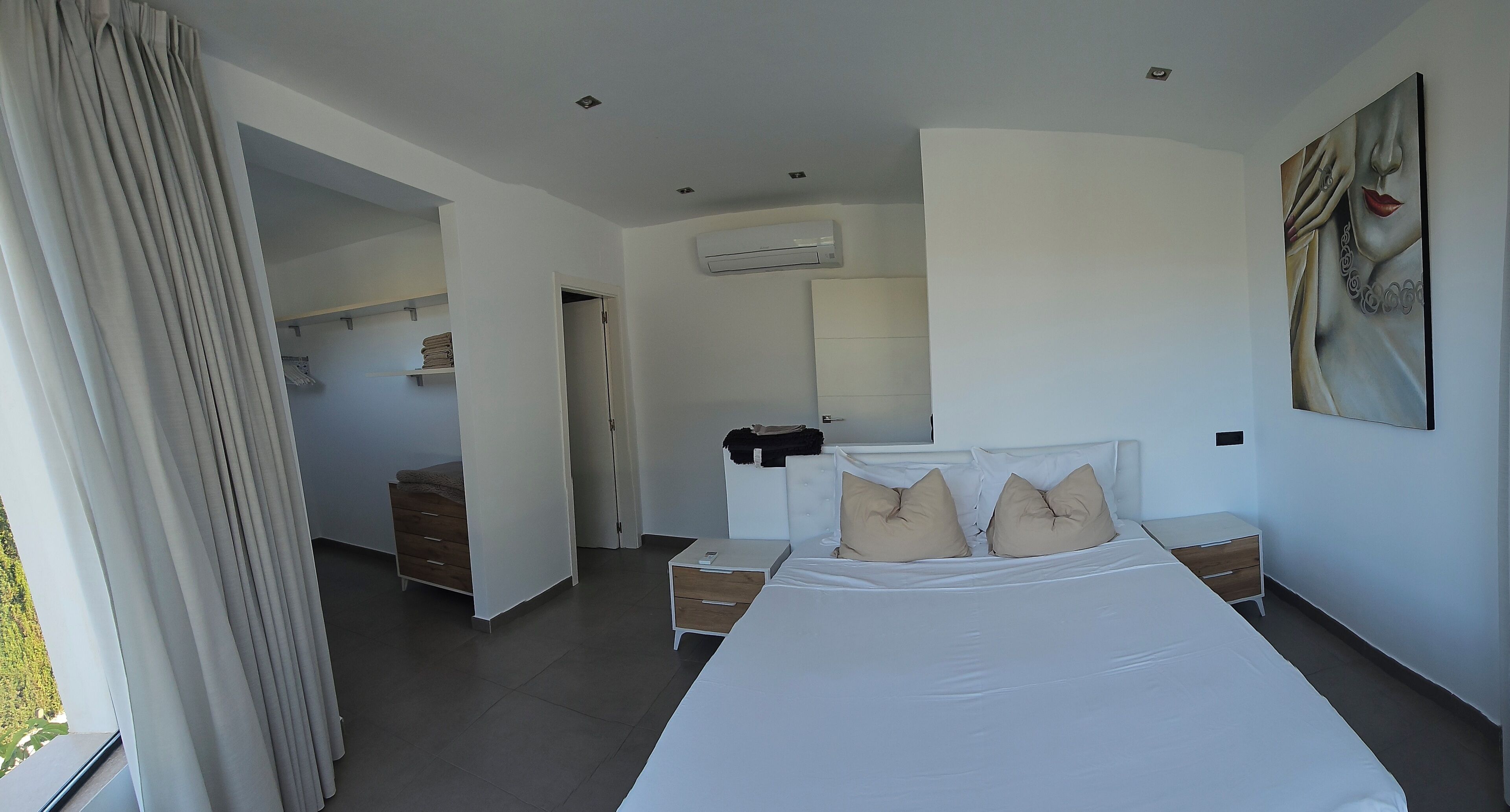 A modern bedroom with a large bed, bedside tables, a wardrobe, and an air conditioning unit.