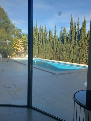 Piscina com deck revestido, cercada por árvores altas e céu claro.