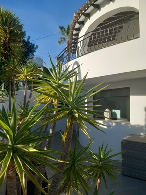 A modern building with a white facade, a balcony with a metal railing, and several palm trees in the foreground. - Luxury 5-Bedroom Villa with a Huge 12.5-Meter Pool – 300 Meters from a Scenic Cove (Cala Baladrar) (Benissa)
