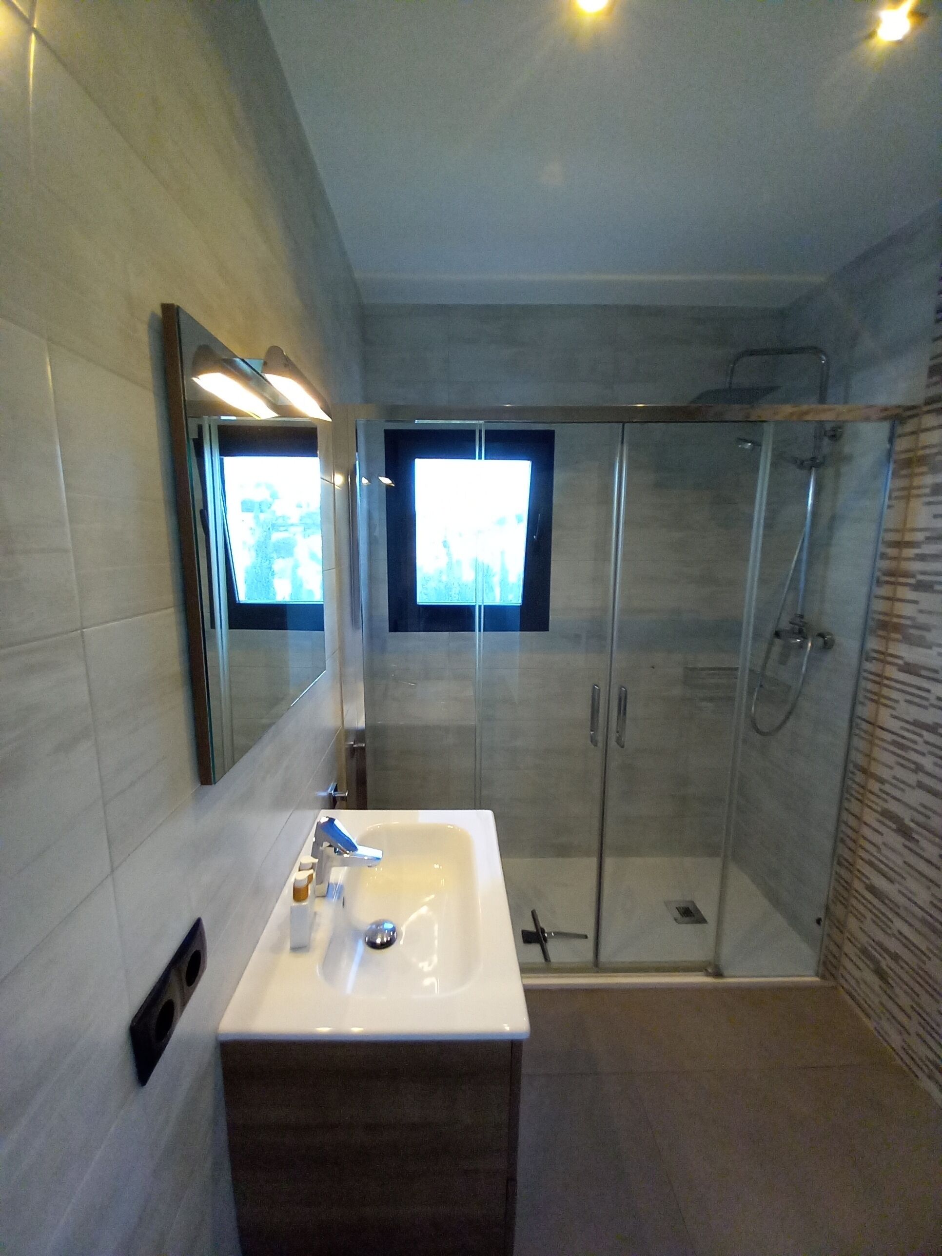 A modern bathroom with a glass-enclosed shower, a large mirror, and a vanity with a sink.