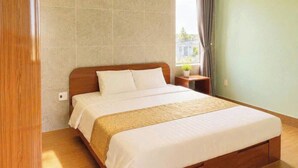 Ein Hotelzimmer mit einem großen Bett, einem Holz-Kopfteil, einem Nachttisch mit Lampe und einem Fenster mit Vorhängen.