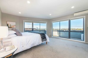 Une chambre avec un grand lit, une table de chevet et une vue sur la ville grâce à de grandes fenêtres du sol au plafond.