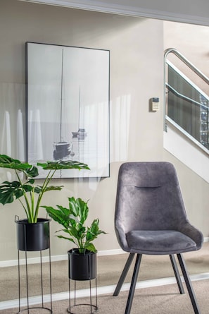 A modern interior with a grey upholstered chair, two potted plants, and a large abstract painting of a sailboat on the wall. - Remuera Elegance - Spacious & Stylish 6-BR House (Auckland)