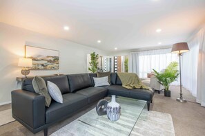 A modern living room with a sectional sofa, a coffee table, and a painting on the wall. - Remuera Elegance - Spacious & Stylish 6-BR House (Auckland)