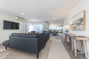 A modern living room with a grey sofa, a flat-screen TV, and a dining area with a table and chairs. - Remuera Elegance - Spacious & Stylish 6-BR House (Auckland)