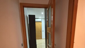 Un couloir étroit, avec une porte en bois sur la droite, qui mène à une pièce où se trouve un lit.