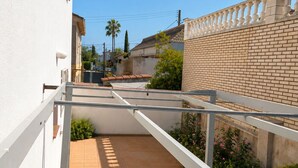 Un étroit couloir extérieur doté d’un sol carrelé, de rampes blanches et d’un mur en briques sur un côté.