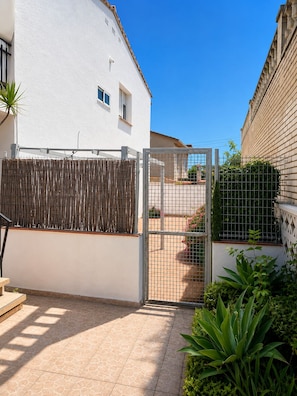 A white building with a gated entrance, a tiled patio, and a bamboo fence. - Mustelier (Cambrils)