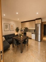 Cocina moderna con comedor, que incluye una mesa y sillas de madera oscura, un refrigerador de acero inoxidable y un microondas.