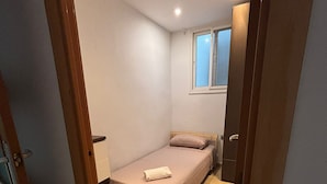 A small, narrow room with a bed, a window, and a door.
