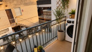 Un balcon avec une chaise, une petite table, une plante en pot et un lave-linge.