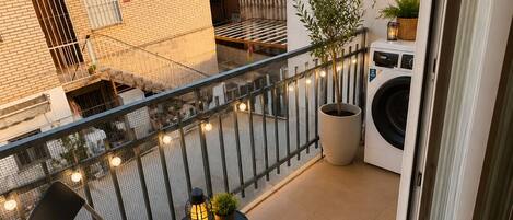 Ein Balkon mit einem Stuhl, einem kleinen Tisch, einem Blumentopf und einer Waschmaschine.