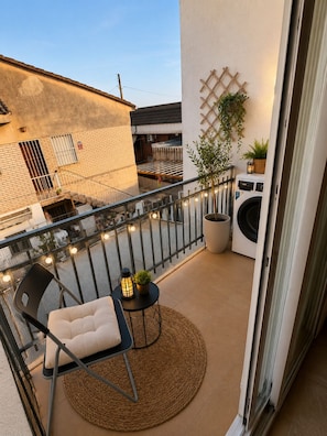 A balcony with a chair, a small table, a potted plant, and a washing machine.