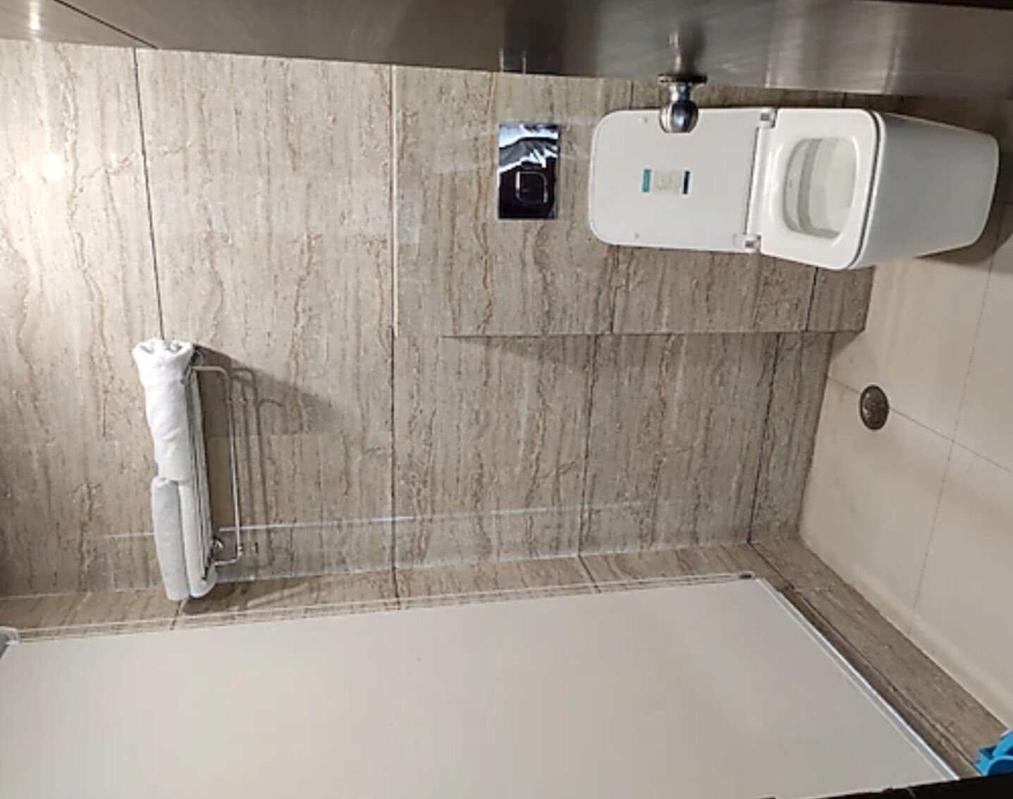 A bathroom with a toilet, a towel dispenser, and a shower area.