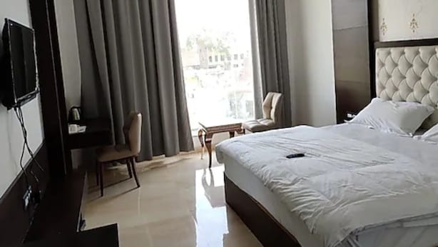 A hotel room with a bed, a desk, a chair, a television, and a window with curtains. - Ramoji Resorts (Hathras)