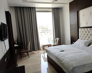 Habitación de hotel con cama, escritorio, silla, televisor y ventana con cortinas.
