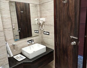 Un baño con lavamanos blanco, encimera oscura y puerta de madera.