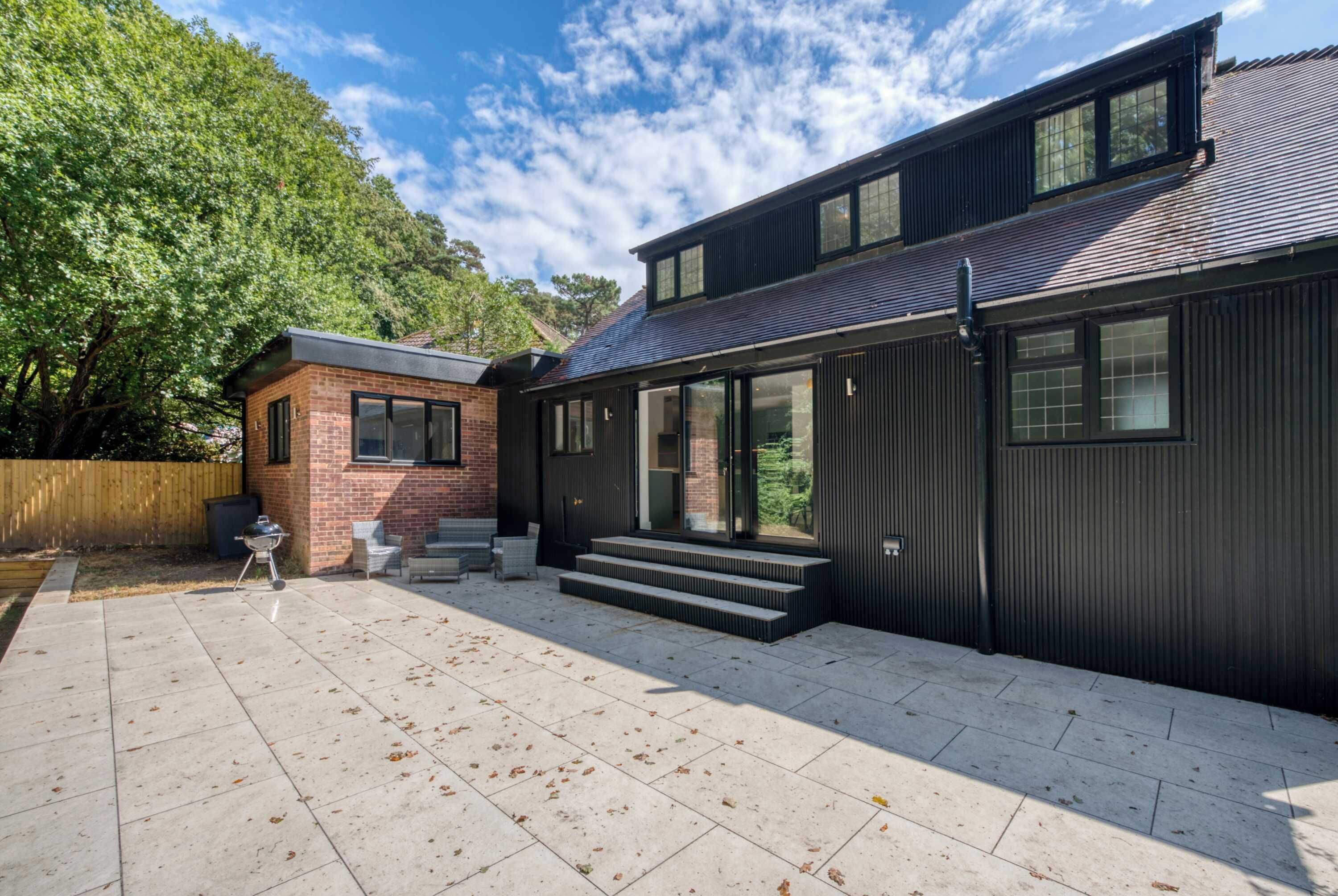 A modern two-story house with a patio area, a barbecue grill, and a wooden fence.