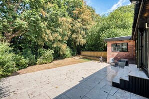 Eine Terrasse mit Backsteinmauer, Grill und Gartenmöbeln.