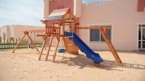 Une structure de jeu en bois comprenant un toboggan, une échelle d’escalade et une tour ressemblant à un château.