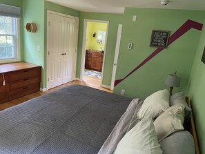 Une chambre à coucher comprenant un lit, une commode et une porte donnant sur une autre pièce.