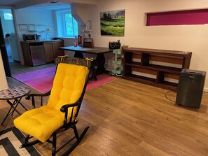 Ein Wohnzimmer mit Schaukelstuhl, Esstisch, Bank und kleinem Kühlschrank.