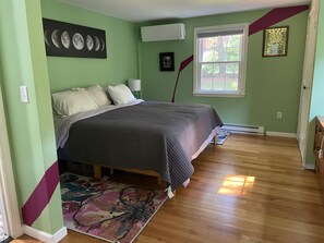 Quarto com cama, janela, ar-condicionado fixado na parede e um quadro emoldurado.