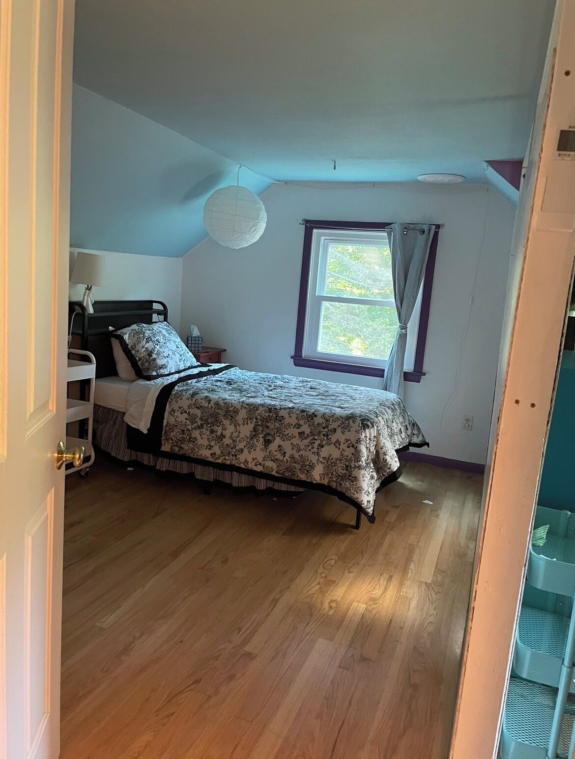 A bedroom with a bed, a nightstand, a lamp, a window with curtains, and a ceiling light fixture.