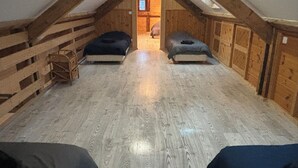 A small attic room with a sloped ceiling, wooden walls, and a central doorway leading to another room. There are two beds against the walls.