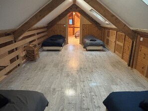 A small attic room with a sloped ceiling, wooden walls, and a central doorway leading to another room. There are two beds against the walls. - Vrbo Property (Sainte-Hélène-sur-Isère)