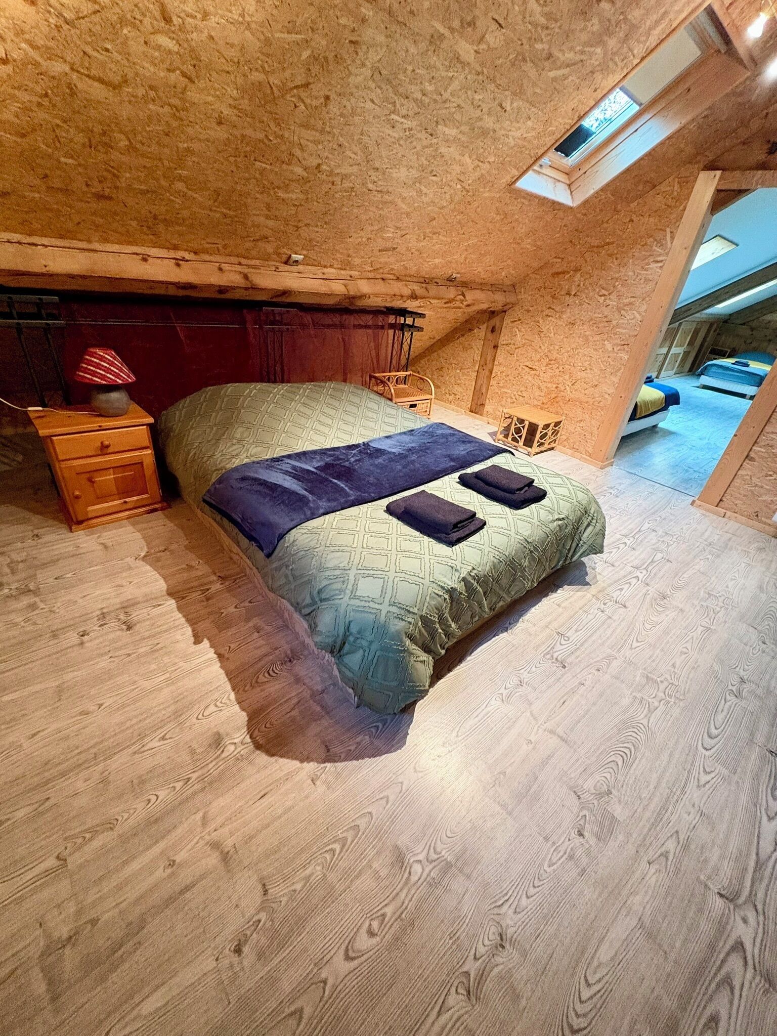 A single bed with a patterned bedspread and pillows, a wooden nightstand, and a small table with a lamp.