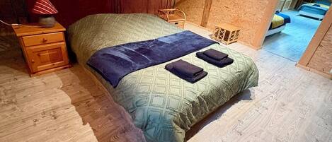 A single bed with a patterned bedspread and pillows, a wooden nightstand, and a small table with a lamp.