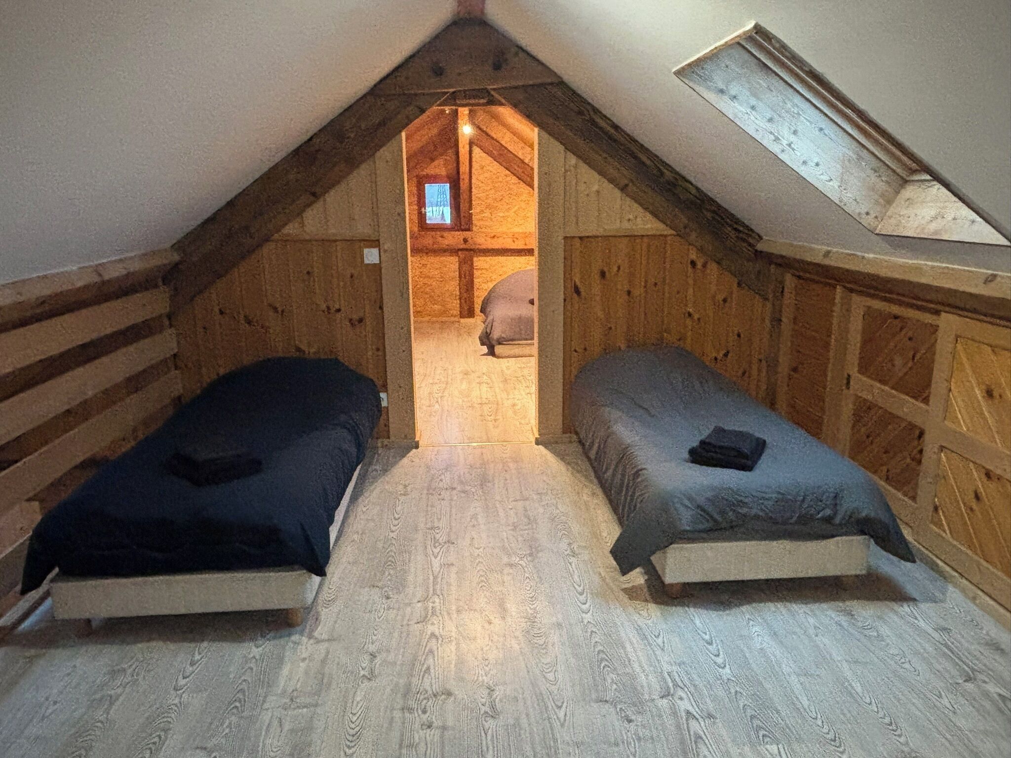 Ett litet sovrum på vinden med två sängar, träväggar, ett sluttande tak och ett takfönster.