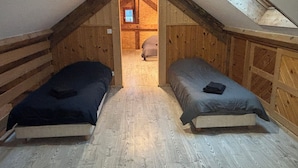 A small attic bedroom with two beds, wooden walls, a sloped ceiling, and a skylight.