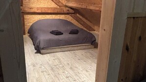 A small attic bedroom with a sloped ceiling, a single bed, and a wooden floor.