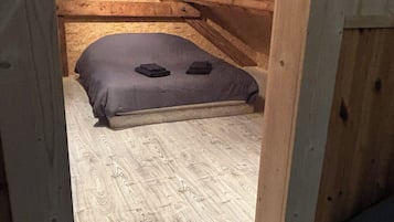 Quarto de sótão pequeno, com teto inclinado, uma cama de solteiro e chão de madeira.