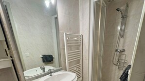 A bathroom with a sink, mirror, shower, and a towel rack.