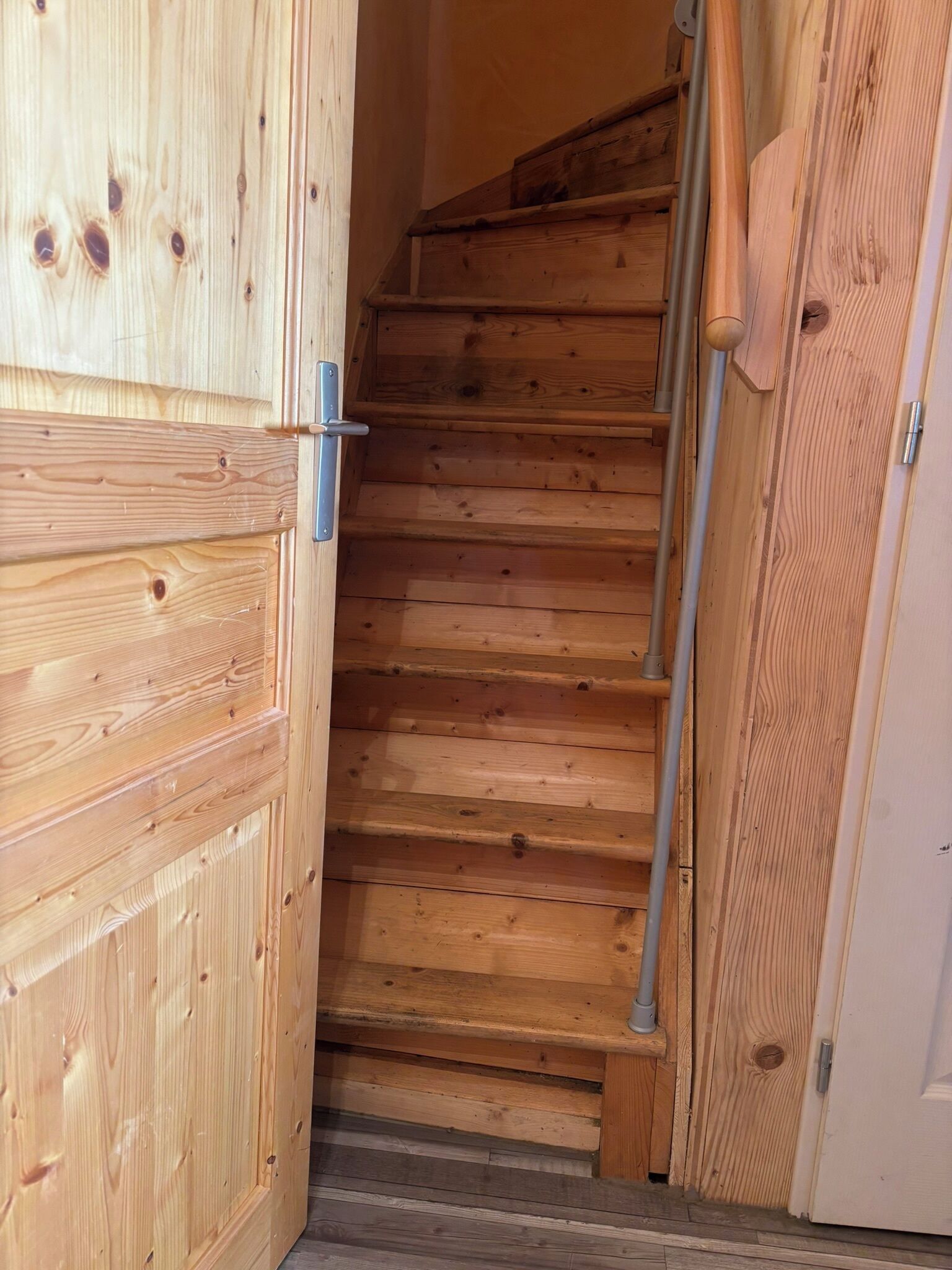 Eine Holztreppe führt zu einer Tür mit einem Metallgriff.