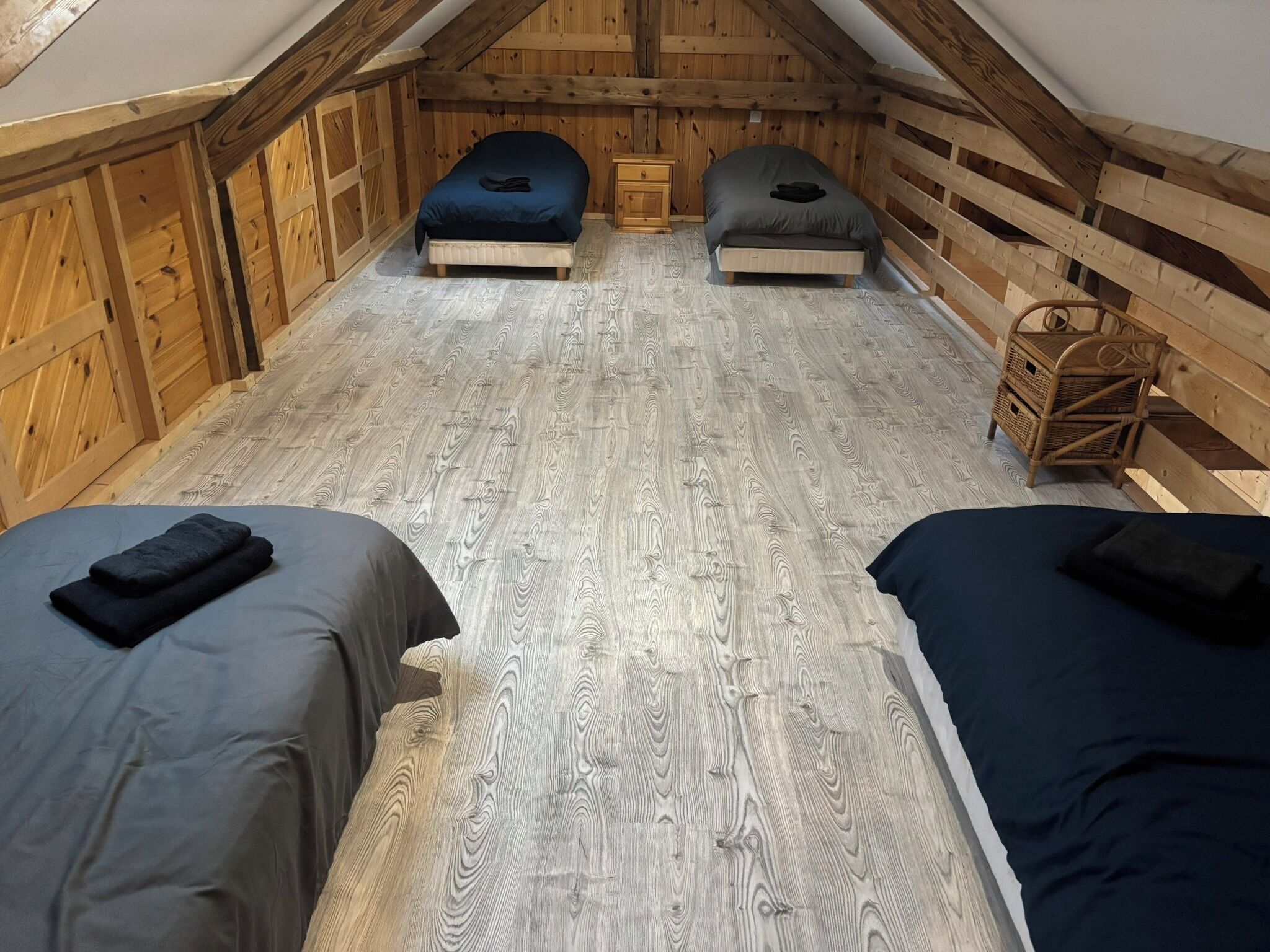 A small, cozy attic bedroom with two beds, a wooden floor, and a small wooden chair.